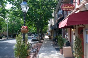 Sidewalk lined with restaurants, shops, benches, and mature trees along Farnsworth Avenue in downtown Bordentown City NJ