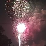Fireworks lighting up the night sky above a community gathering during a summer celebration