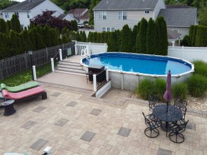Above-ground swimming pool with attached deck, paver patio, outdoor seating, and landscaping in the backyard of a Hamilton NJ home.