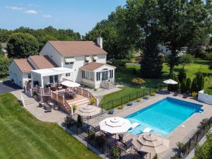 Hamilton NJ home with inground pool, multi-level deck, outdoor seating, landscaping, and open lawn space in the backyard.