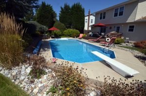 Inground swimming pool with backyard deck, lounge chairs, landscaping, and outdoor seating at a Hamilton NJ home.