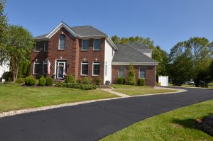 Two-story brick colonial home in Hamilton Square NJ with mature landscaping and a long driveway.