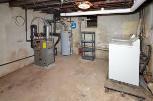 Basement mechanical area with furnace, water heater, exposed plumbing, and foundation walls representing components commonly evaluated during a home inspection.