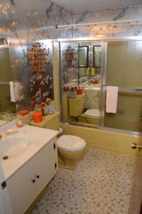Original full bathroom in a Cherry Hill NJ home with vintage tile flooring, patterned wall covering, older fixtures and tub-shower enclosure.