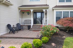 Welcoming front entrance of a Hamilton NJ home with a covered porch, brick paver walkway, landscaping, and flowering plants.