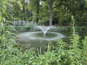Pond with fountain and white footbridge surrounded by trees and gardens at Sayen House and Gardens in Hamilton Township NJ