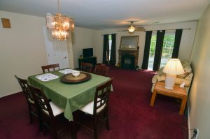 Well-maintained living and dining room in Jackson NJ with burgundy carpeting, brick fireplace, traditional lighting and older interior finishes.