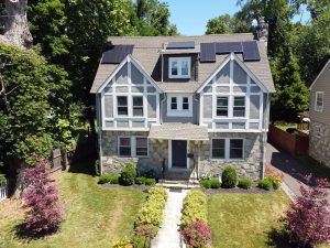 Aerial front view of a distinctive stone and Tudor-style home in the Glen Afton section of Trenton NJ with mature landscaping and solar panels.