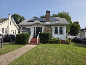 Front exterior of a Hamilton Township NJ estate property with white siding, brick chimney, solar panels and front steps.