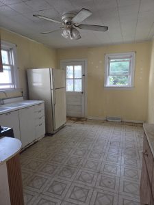 Older kitchen in a Hamilton Township NJ estate property with dated wood cabinetry, patterned flooring, double sink, and gas range.