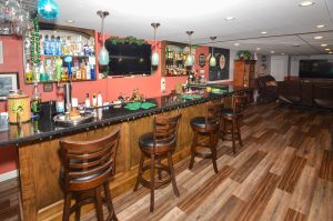 Finished basement in a Hamilton Township NJ home featuring a custom wood pub style bar, bar seating, wall mounted televisions, and recreation space.