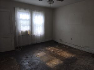 Bedroom in a Hamilton Township NJ estate property with hardwood floors, ceiling fan, window air conditioner and visible wear before an as is sale.