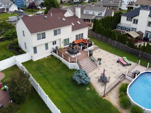 Aerial view of a Hamilton Township NJ home with a large deck, expansive paver patio, backyard lawn and above-ground pool.
